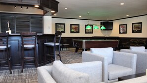 A bar area with a pool table, cushioned seating, and framed artwork on the walls.