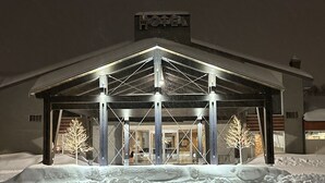 A hotel entrance with a covered lobby, snow-covered surroundings, and illuminated trees.