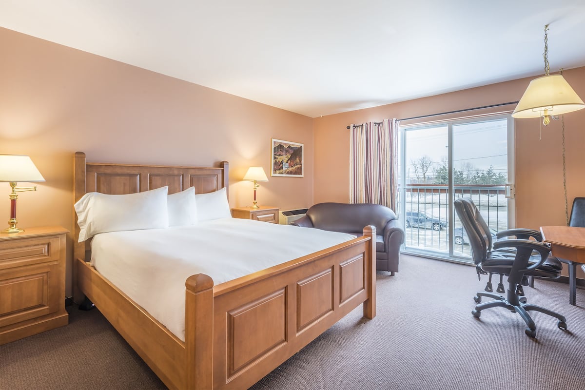Een hotelkamer met een houten bed, twee nachtkastjes met lampen, een bureau met stoel, en een groot raam met gordijnen.