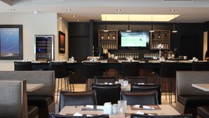 A restaurant with booths and tables, a bar area with bottles and glasses, and a TV screen displaying a sports game.