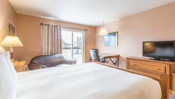 A hotel room with a large bed, a desk, a chair, a television, and a window with curtains.