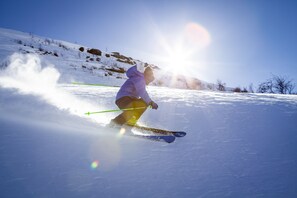Iemand skiënd op een met sneeuw bedekte helling, met een heldere lucht en zon op de achtergrond.