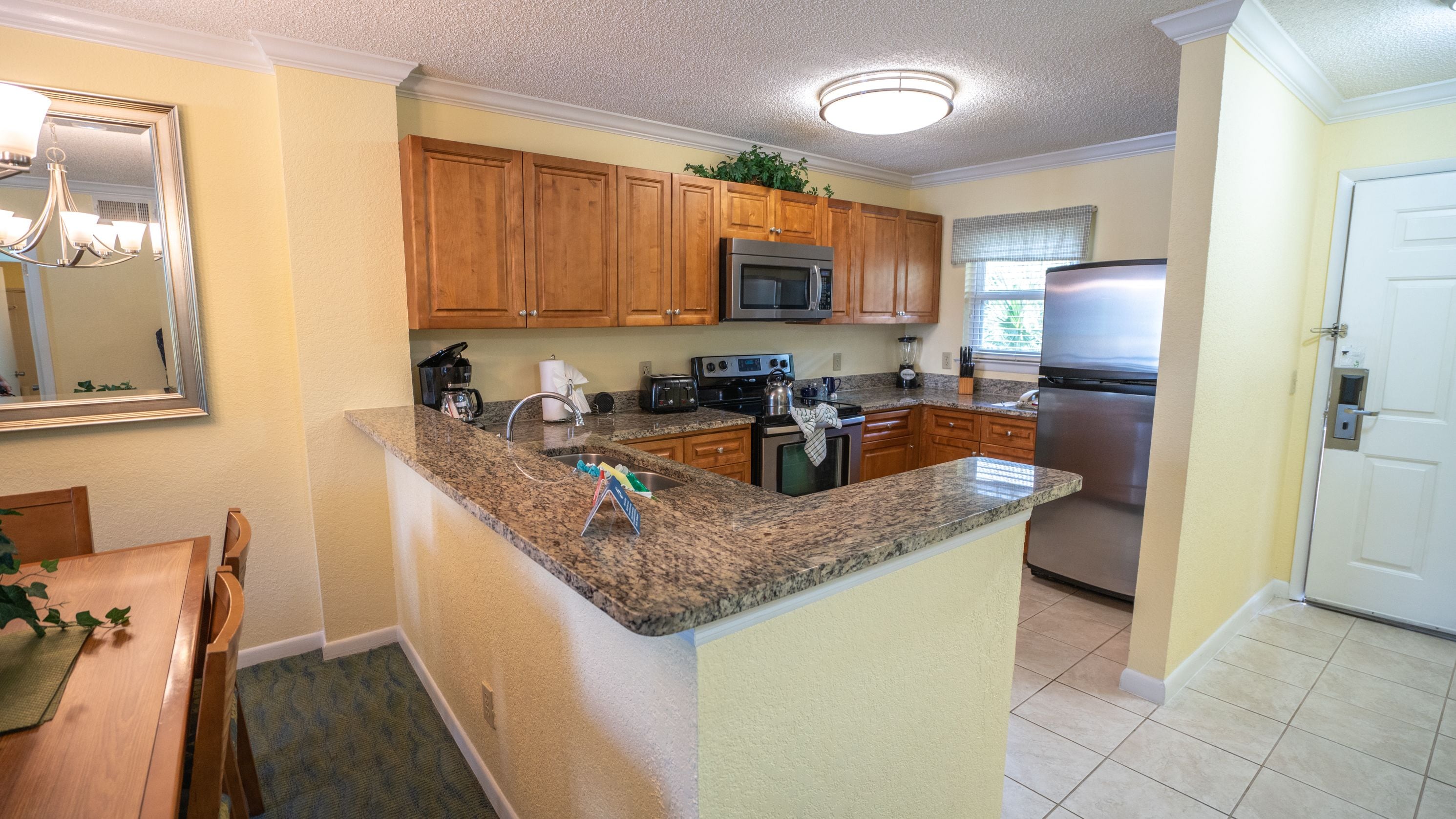 A modern kitchen with granite countertops, wooden cabinets, stainless steel appliances, and a dining area with a wooden table and chairs.