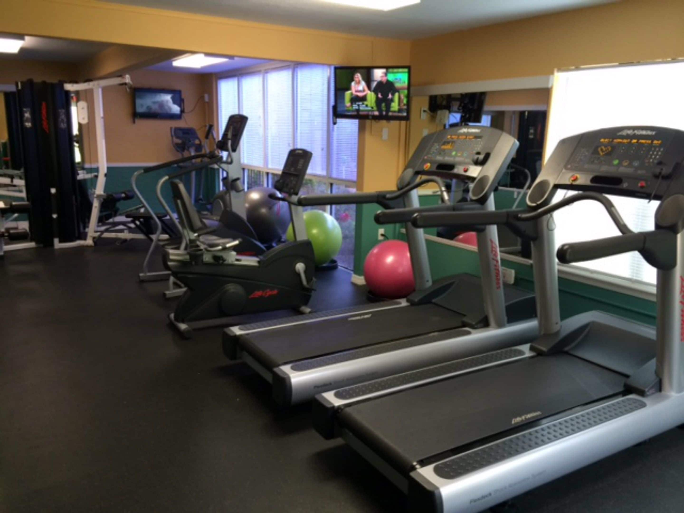 Ein Fitnessstudio mit Laufbändern, Gymbällen und einem Fernseher, der eine Fernsehsendung zeigt.