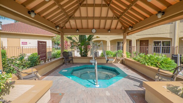 Un espace extérieur abrité avec une piscine, des chaises longues, une horloge et un panneau indiquant les règles du spa et interdisant les plongeons.