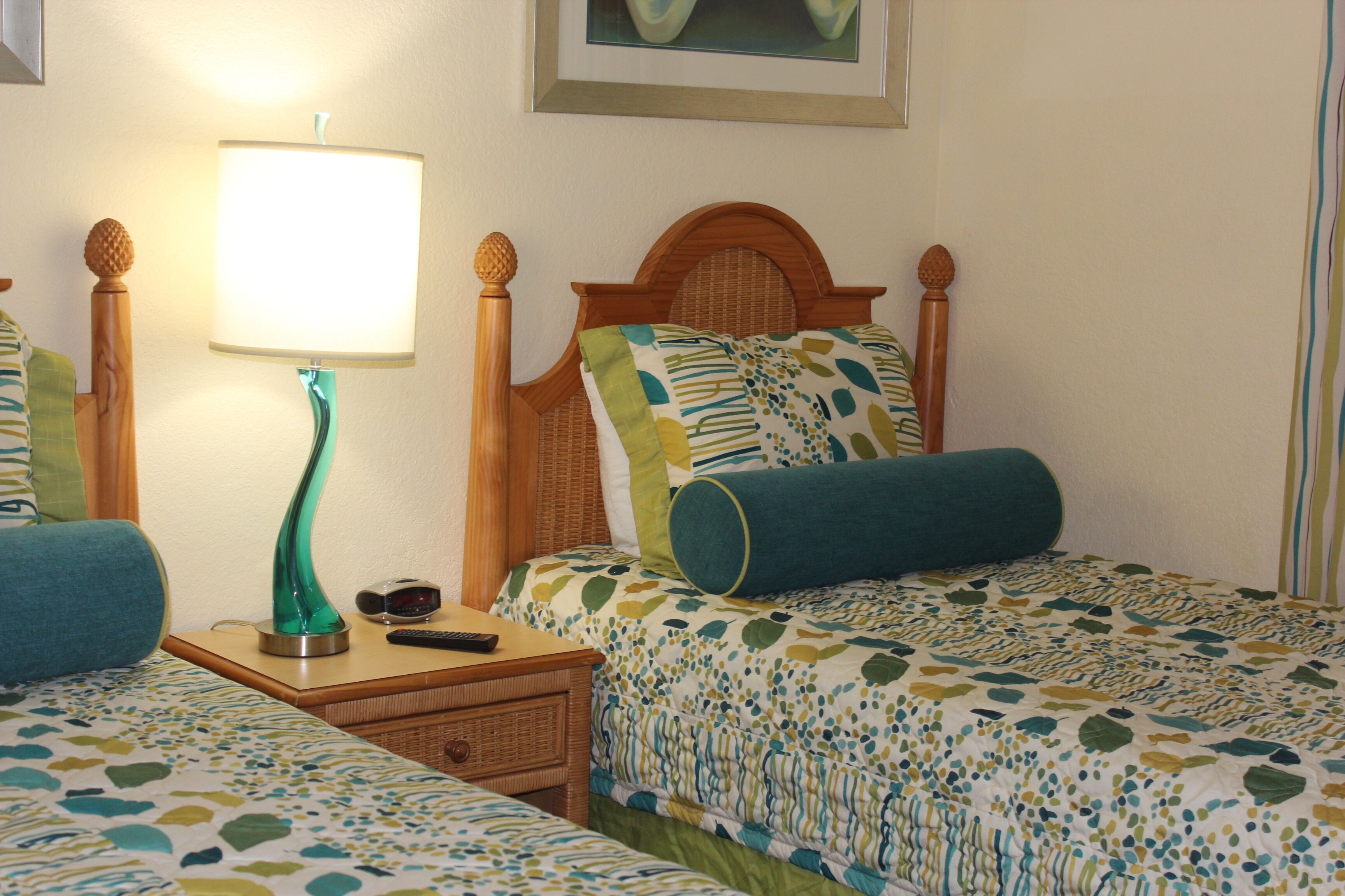 A hotel room with two beds, a nightstand with a lamp, a remote control, and a framed picture on the wall.