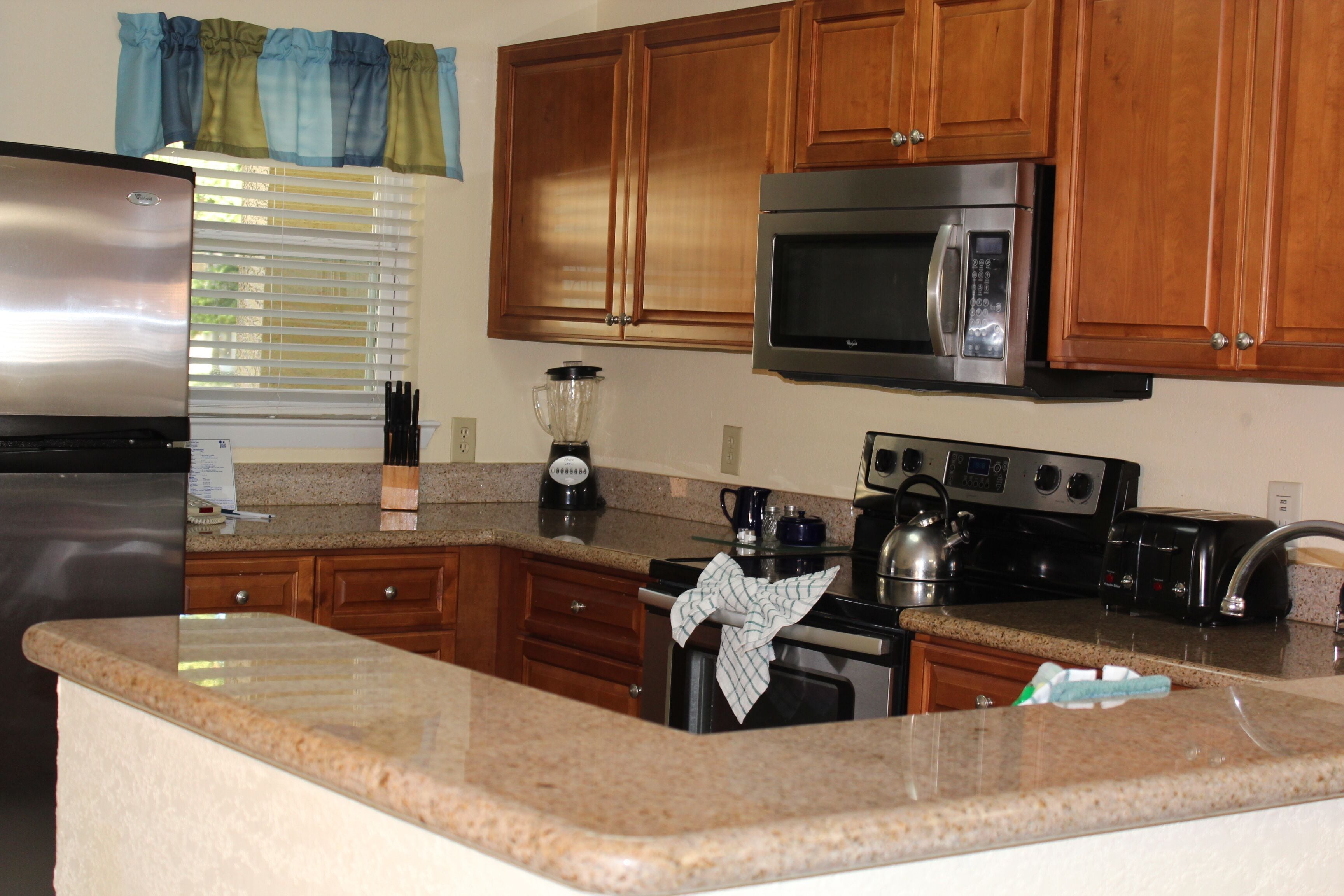 A kitchen with wooden cabinets, a stainless steel refrigerator, a microwave, a stove, and a blender.