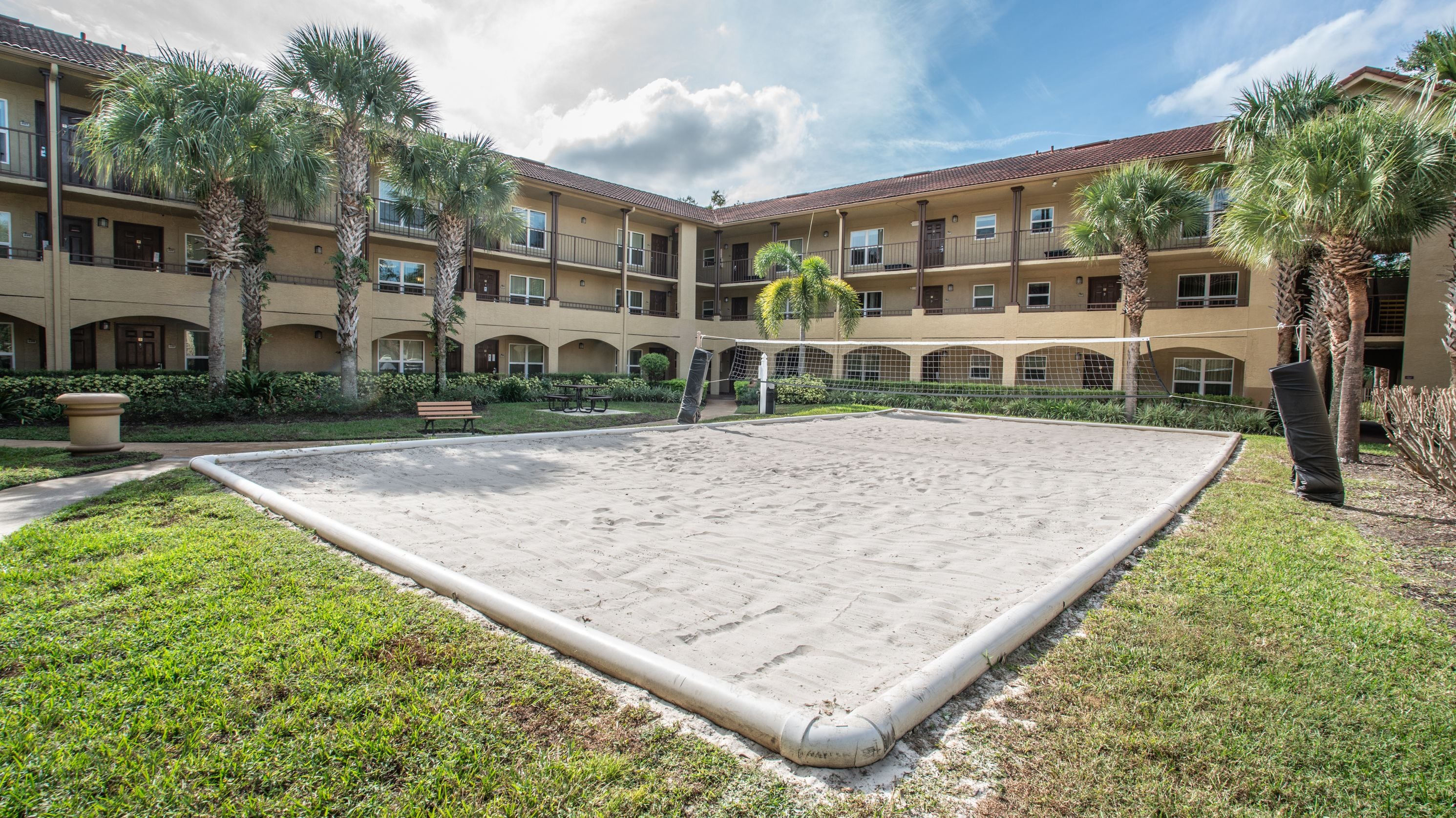 A courtyard with a volleyball net, palm trees, and a building with multiple balconies.