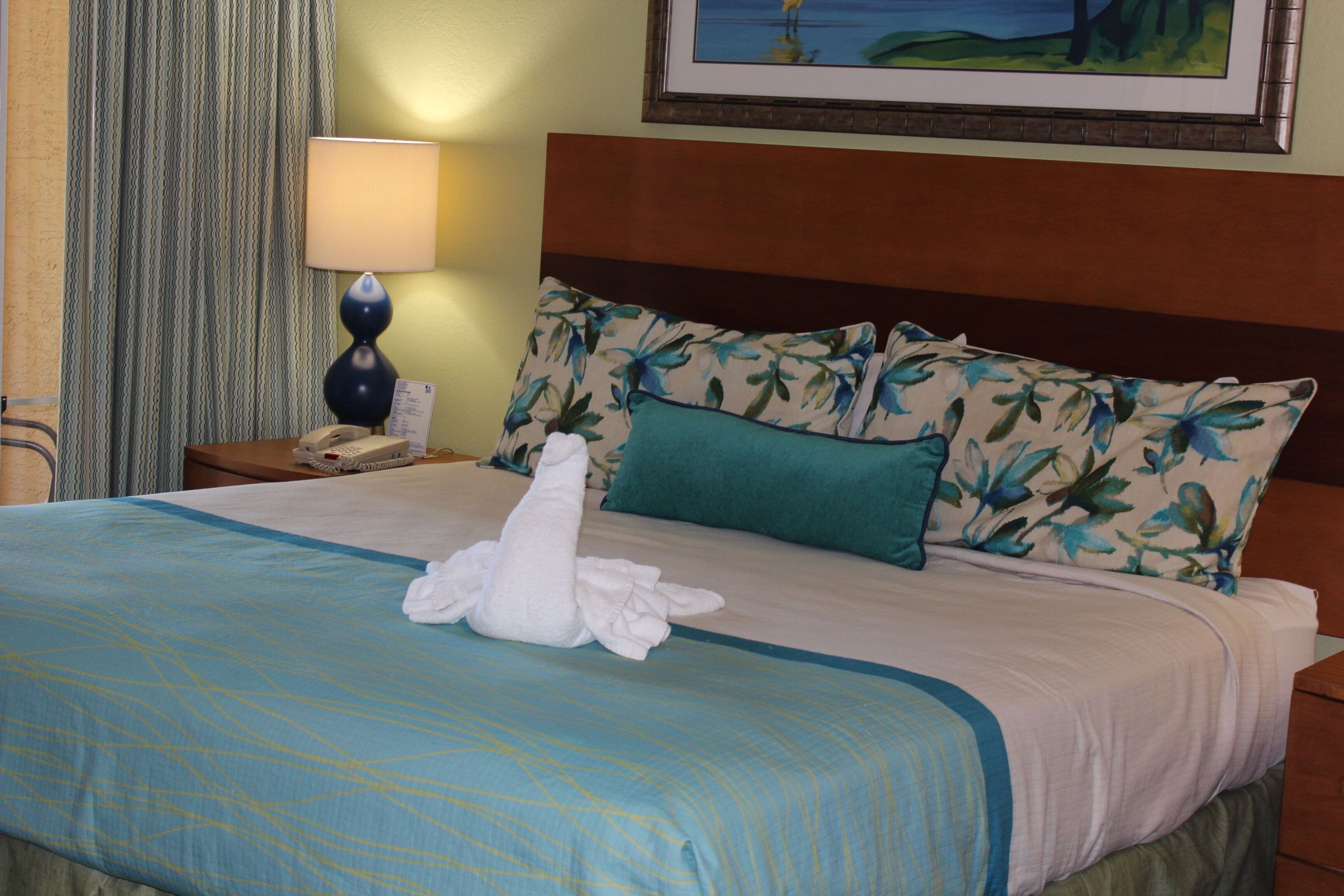 A neatly made bed with a blue and white bedspread, a green pillow, and a white towel.