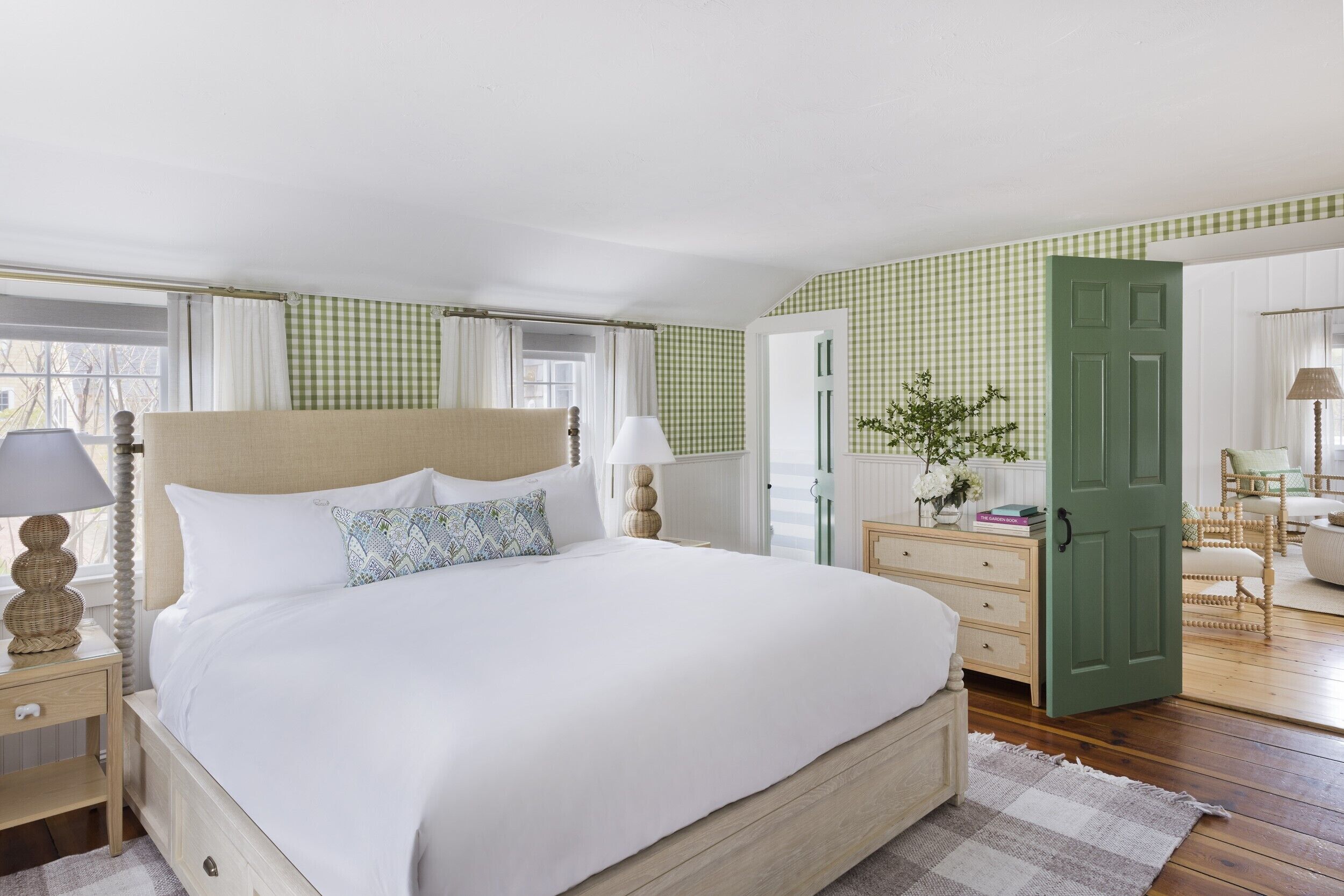 A neatly arranged bedroom with a large bed, bedside tables, a dresser, and a green door.