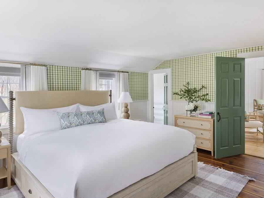 A neatly arranged bedroom with a large bed, bedside tables, a dresser, and a green door.