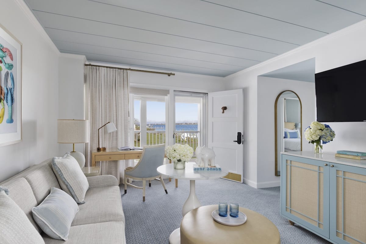 A modern hotel room with a sofa, a desk, a round table, and a view of the sea.