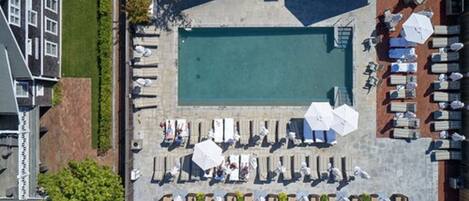 An aerial view of a rooftop pool area with lounge chairs and umbrellas, surrounded by buildings.