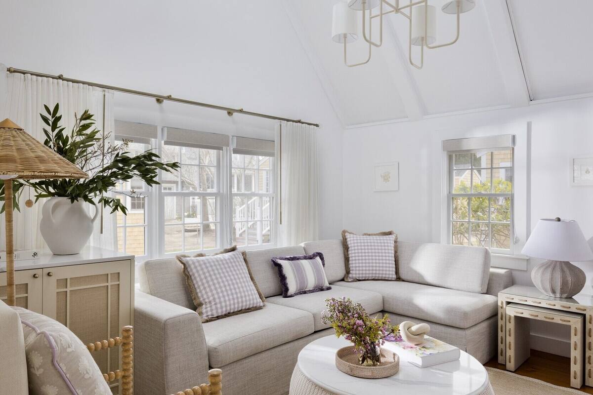 A spacious living room with a high ceiling, large windows, a round white coffee table, and a comfortable seating area.
