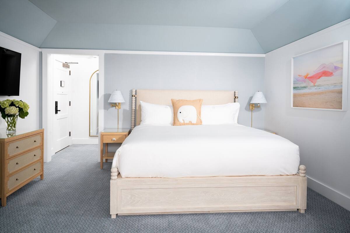 A bedroom with a bed, bedside tables, a dresser, a TV, and a painting on the wall.