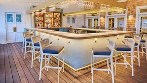 A bar area with a counter, bar stools, and hanging light fixtures. - White Elephant Hotel (Nantucket)