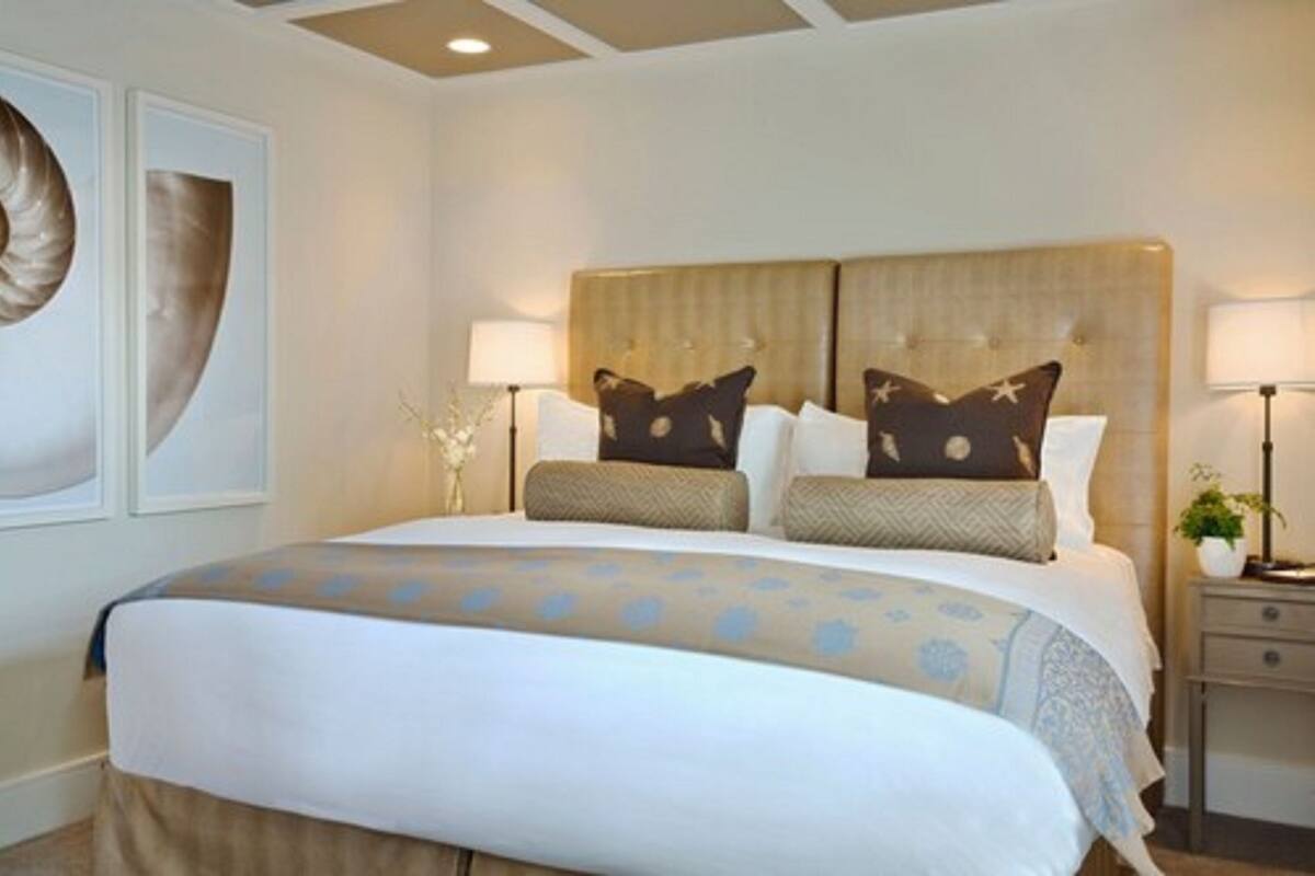 A hotel room with a large bed, two bedside tables, a nightstand, and a wall-mounted lamp.