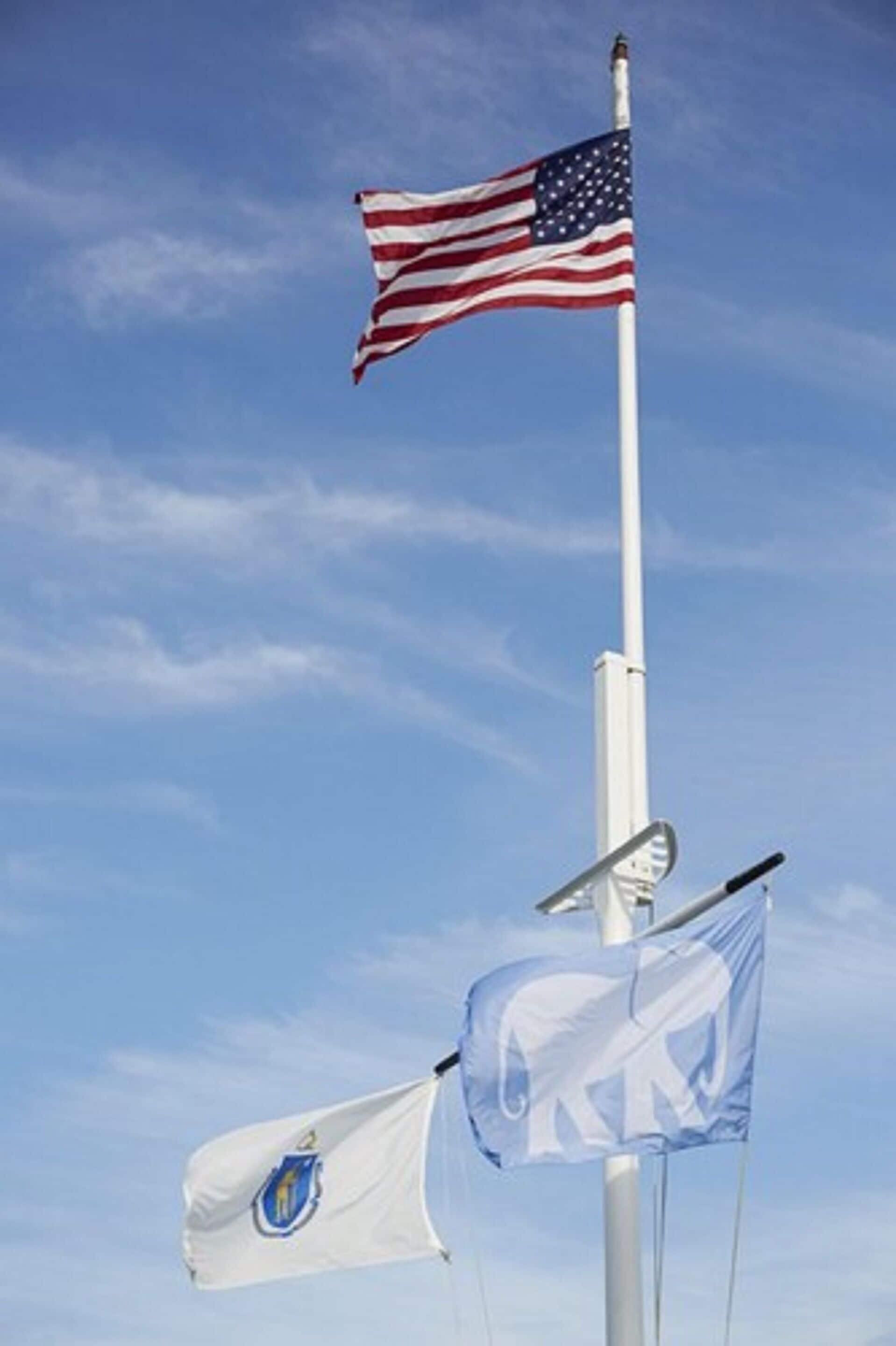An American flag and a flag with a blue and white emblem on a flagpole against a clear sky.