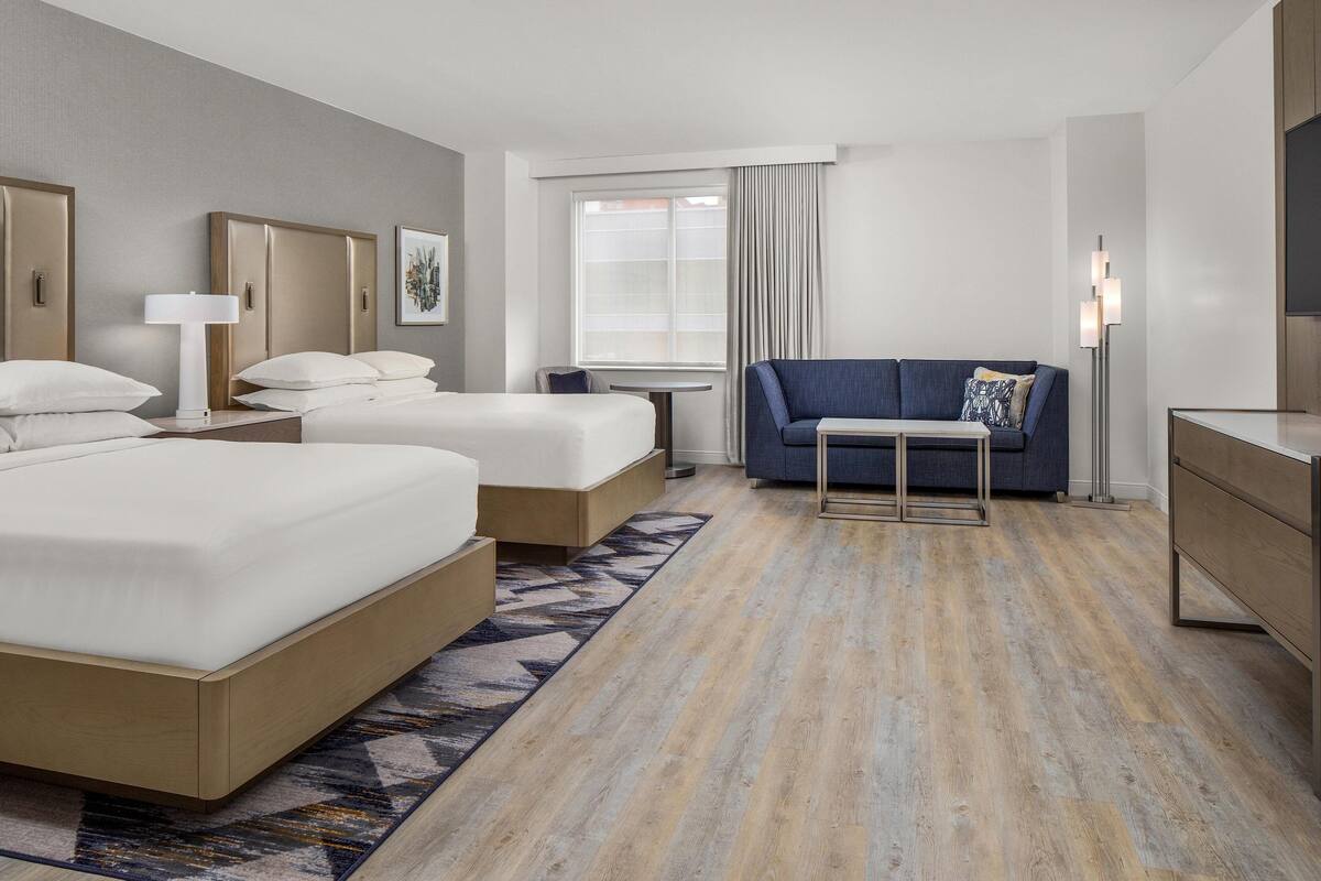 A hotel room with two beds, a sofa, a small table, and a floor lamp.