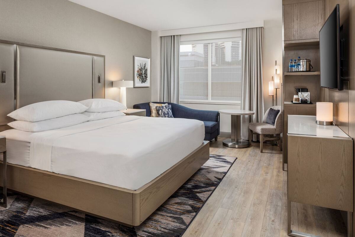 A hotel room with a large bed, a desk, a chair, a TV, and a window with curtains.