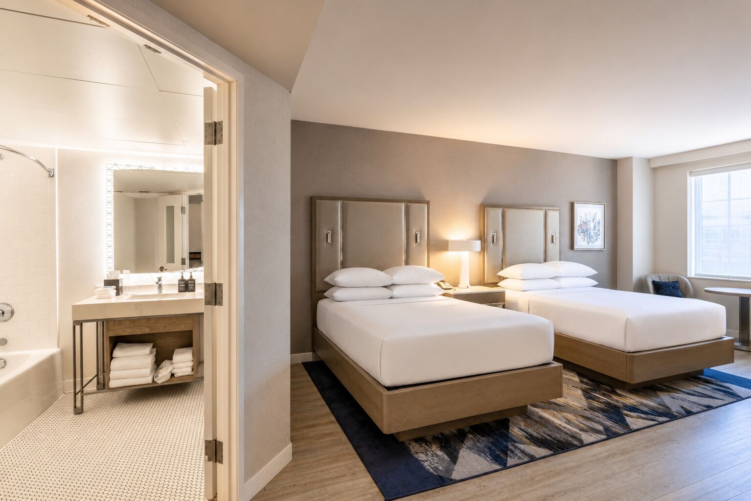 A hotel room with two beds, a bathroom, and a desk.