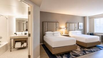 A hotel room with two beds, a bathroom, and a desk.