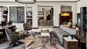 En moderne hotellobby med et geometrisk mønstret tæppe, moderne møbler og en dekorativ vægpanel.