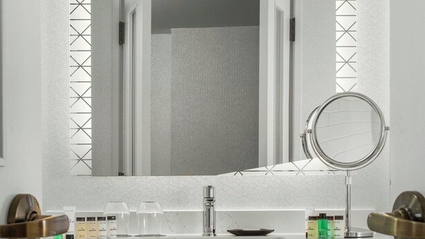 A modern bathroom with a white vanity, a mirror, and a wooden shelf with folded towels. - Sheraton Duluth Hotel (Duluth)