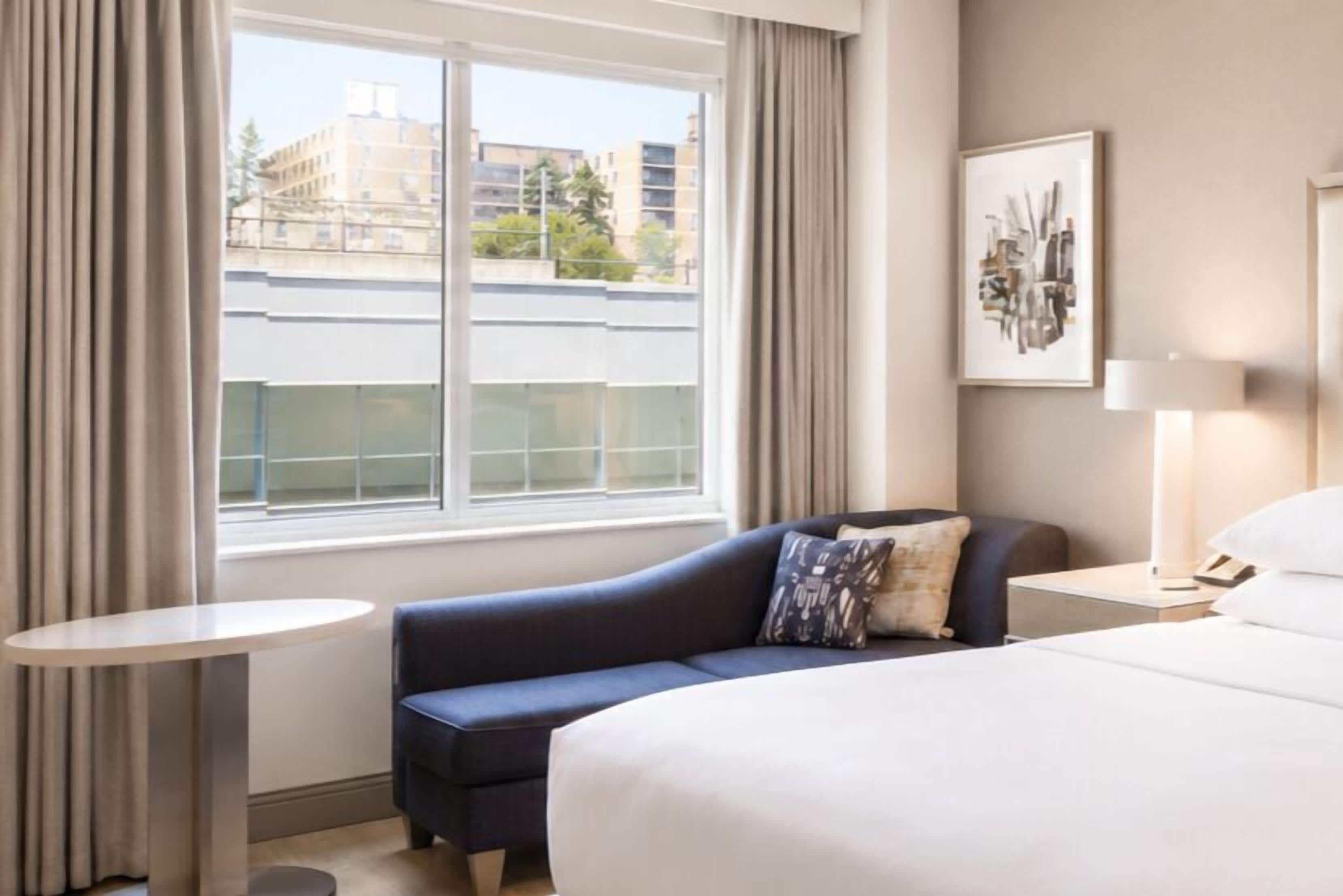 A hotel room with a bed, a sofa, a small table, a lamp, and a window with curtains.