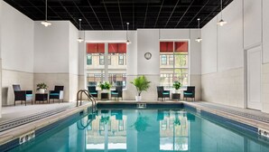 Et indendørs swimmingpool med klart vand, omgivet af liggestole og krukker med planter.