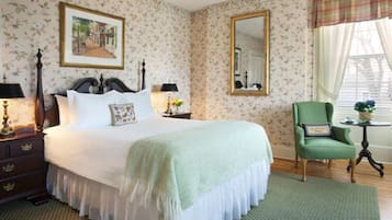 A neatly arranged bedroom with a large bed, a green armchair, a small table with a plant, and a mirror on the wall.