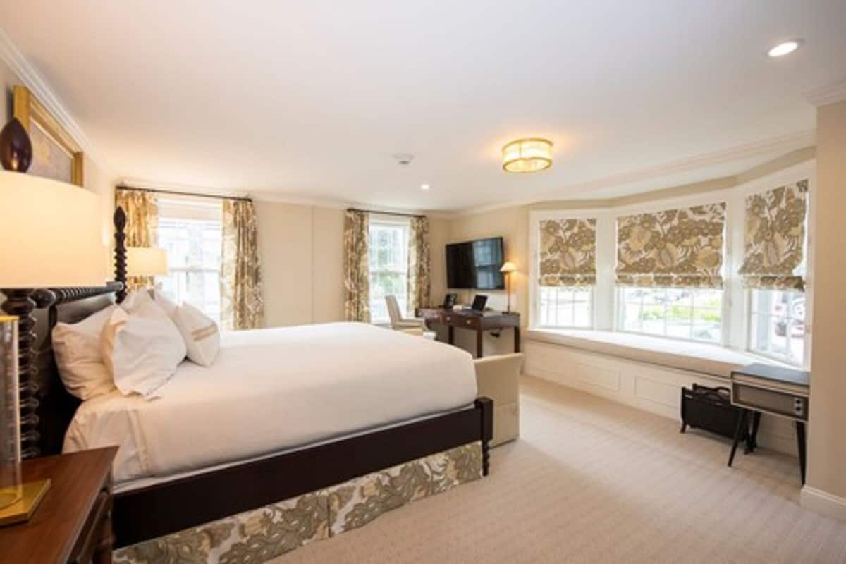 A spacious bedroom with a large bed, a desk, and a television.