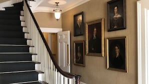 A grand staircase with a dark wooden finish and white balusters, leading to a room with beige walls and framed portraits. - Jared Coffin House (Nantucket)