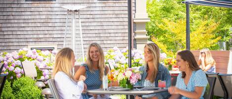 Un patio al aire libre con cuatro personas sentadas en una mesa, rodeado de sombrillas a rayas y arreglos florales.
