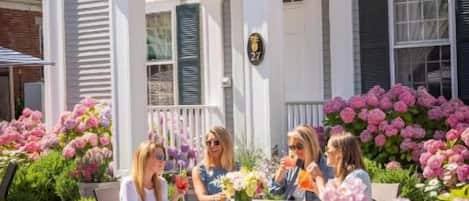 A white building with a porch, surrounded by pink and purple flowers.