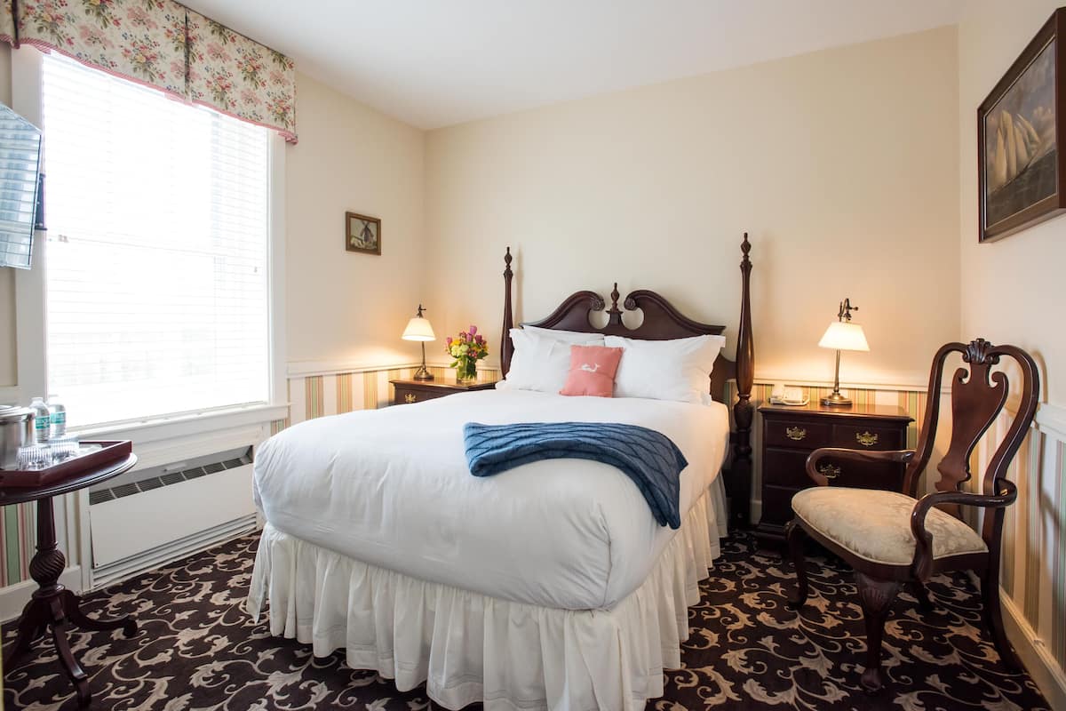 A neatly arranged bedroom with a large bed, two bedside tables with lamps, a chair, and a window with blinds.