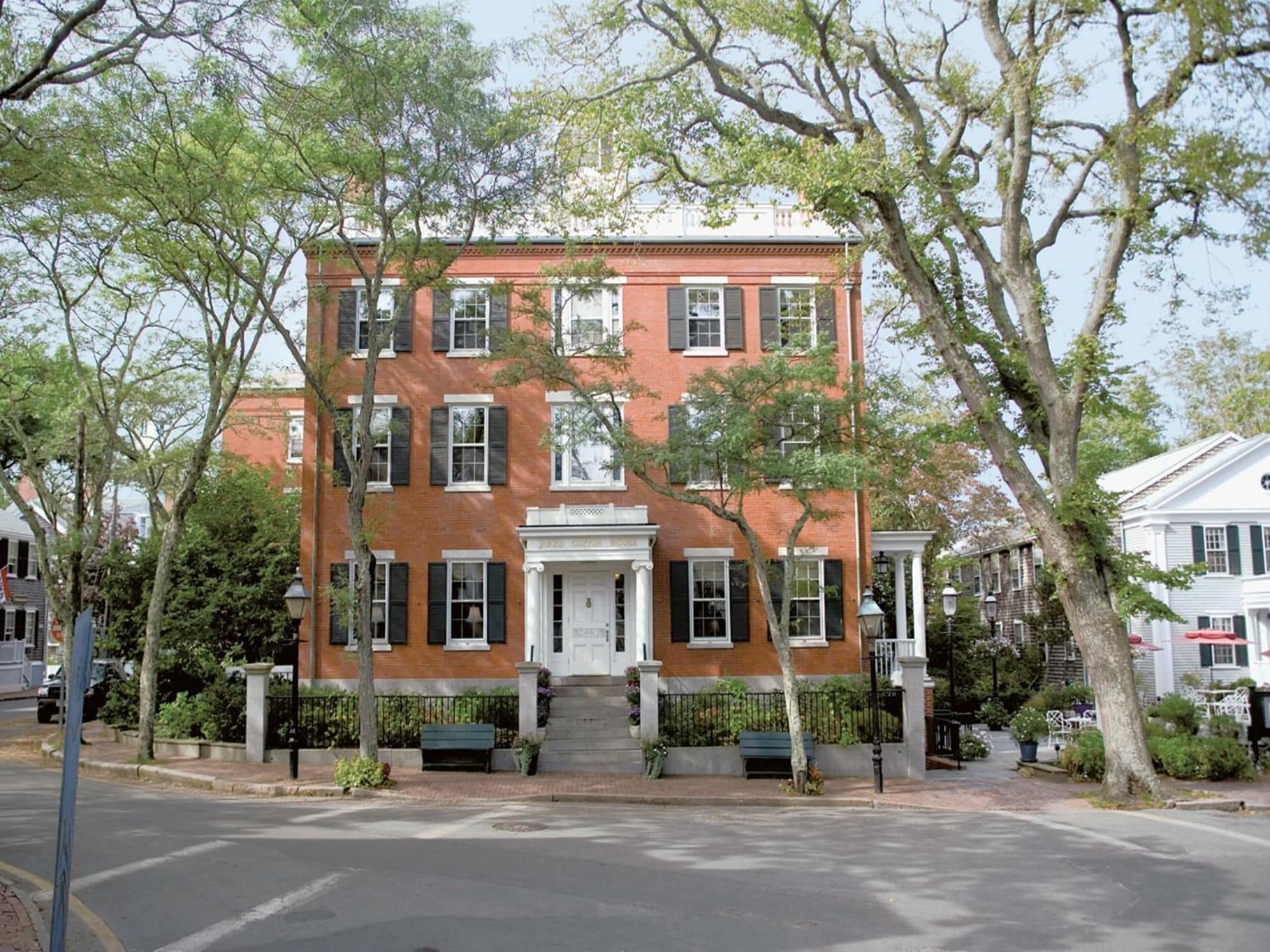 A red brick building with a central entrance, multiple windows, and a small front garden with benches.