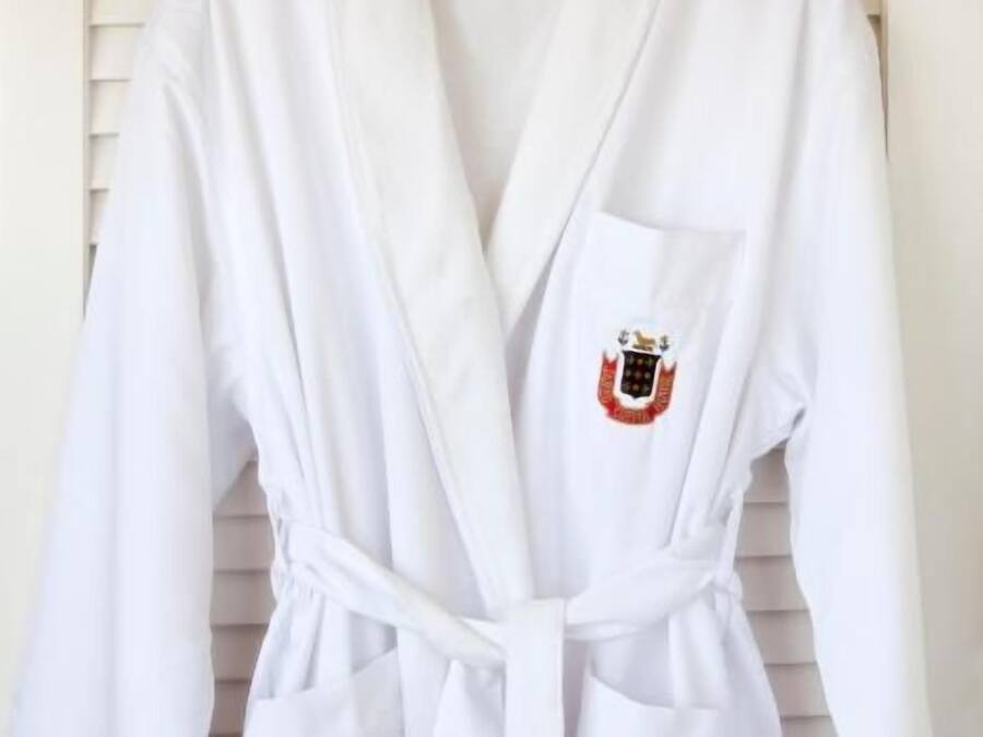 Un banyut blanc amb cinturó i butxaca, penjat en una perxa de fusta.