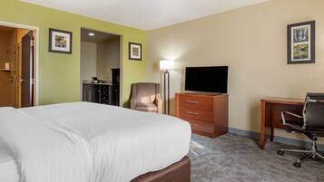 A hotel room with a large bed, a desk, a chair, a TV, and a dresser.