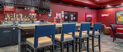 A bar area with a red wall, bar stools, and a variety of liquor bottles.