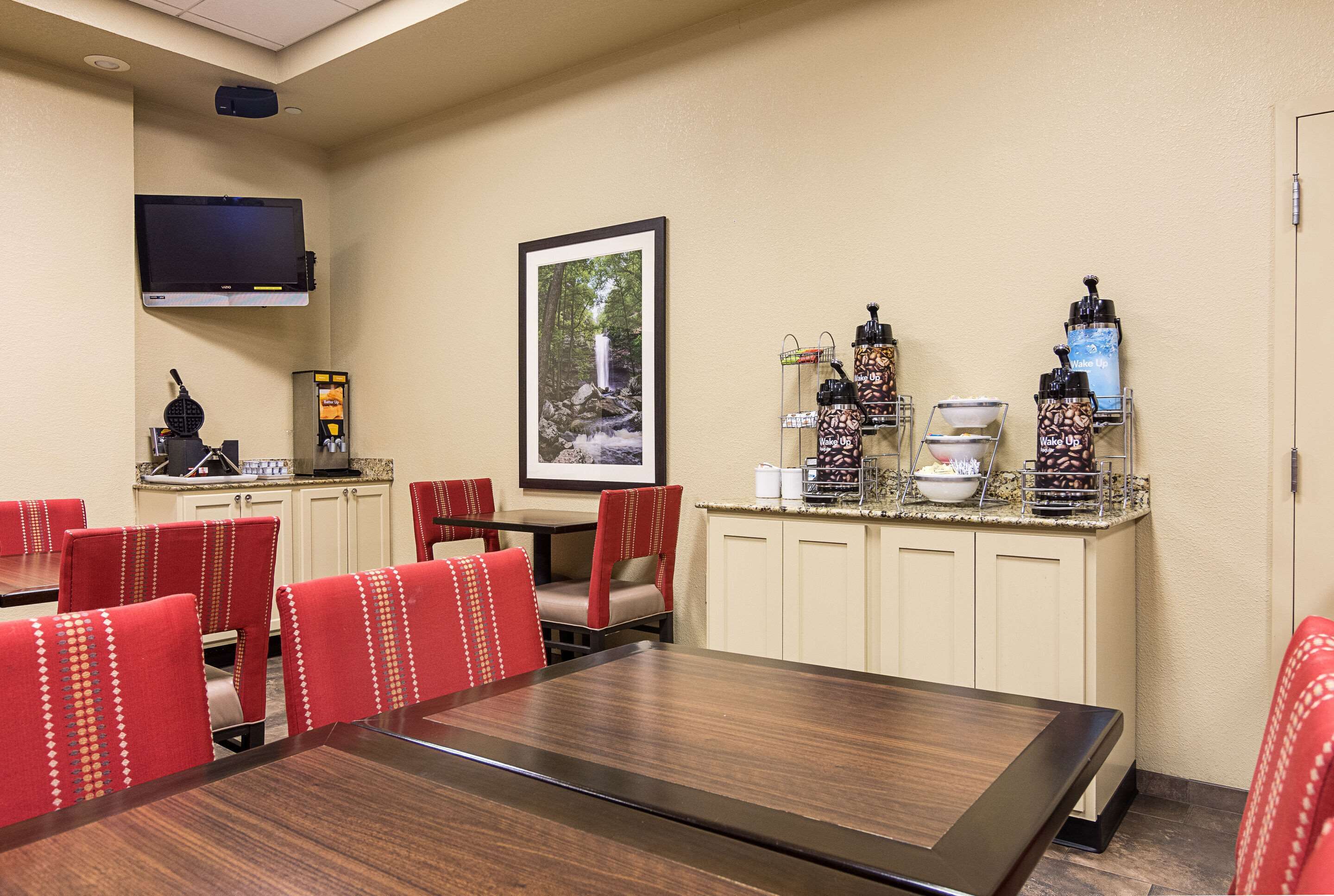 A conference room with a long table and red chairs, a coffee station with various drink dispensers, and a framed picture of a waterfall on the wall.