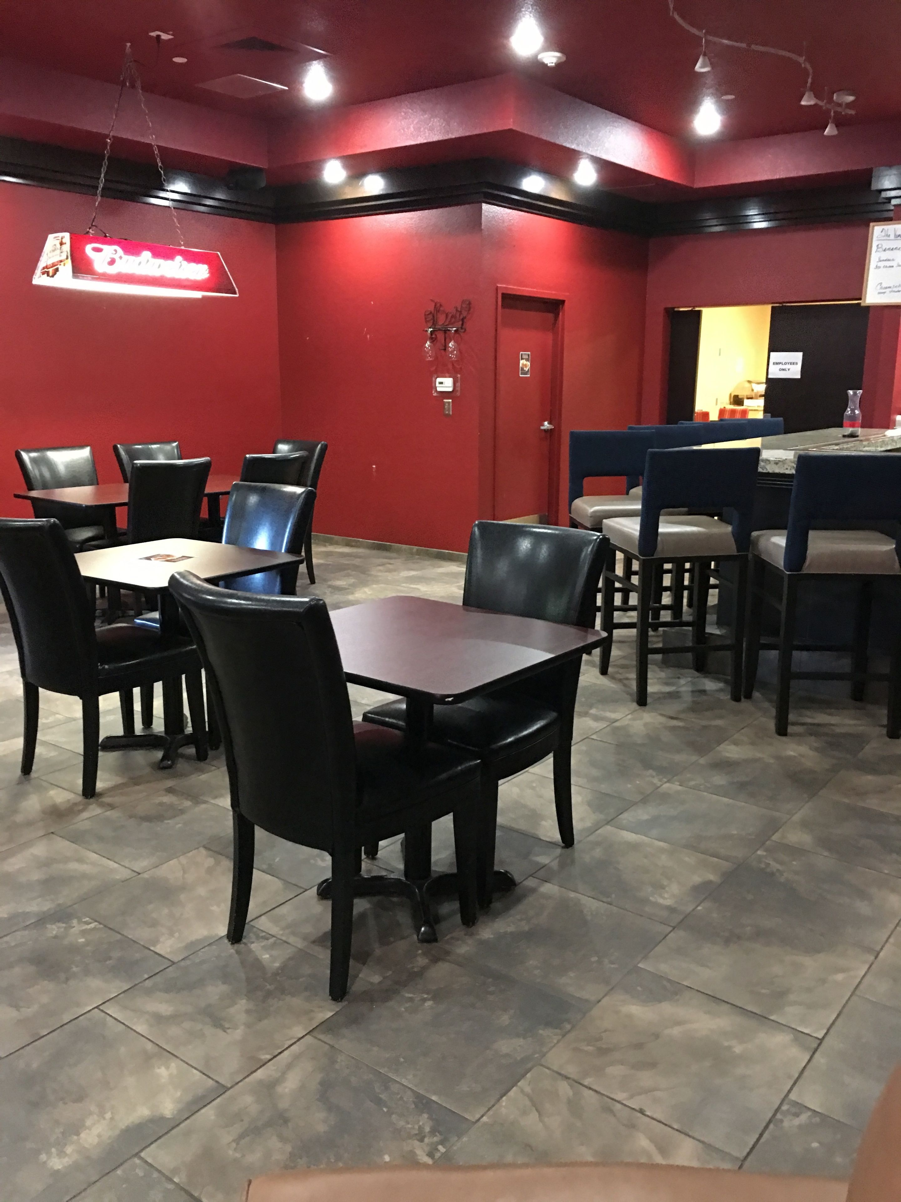 L’intérieur d’un restaurant présente des murs rouges, des chaises noires et bleues, ainsi que des tables. Un panneau néon est placé au-dessus de l’entrée, et une porte porte l’inscription « RESERVÉ AU PERSONNEL ».