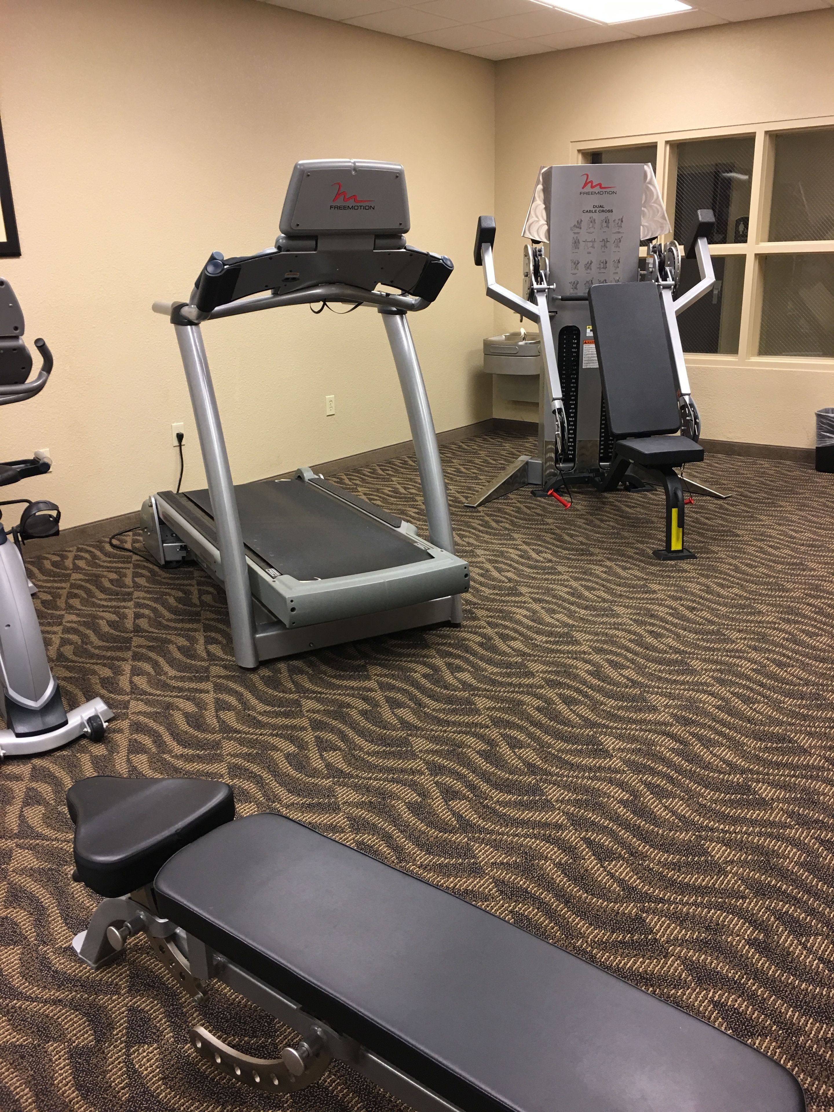 Ein Fitnessraum mit Laufband, Crosstrainer und einer Bank.