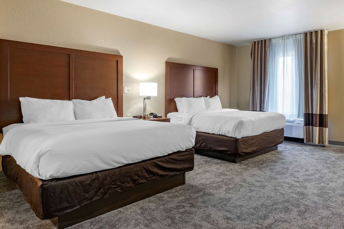 A hotel room with two beds, a nightstand with a lamp, a telephone, and a window with curtains.