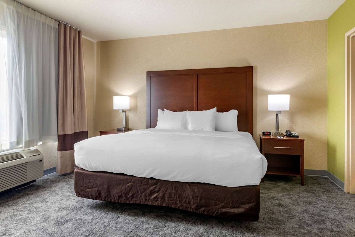 A hotel room with a large bed, two bedside tables with lamps, a heater, and a window with curtains.