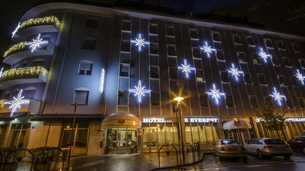A hotel with multiple floors, star-shaped lights on the facade, and a visible entrance with a canopy. - Hotel Everest (Trento)