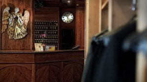 A wooden reception desk with a clock and a shelf of bottles. - Hotel Everest (Trento)