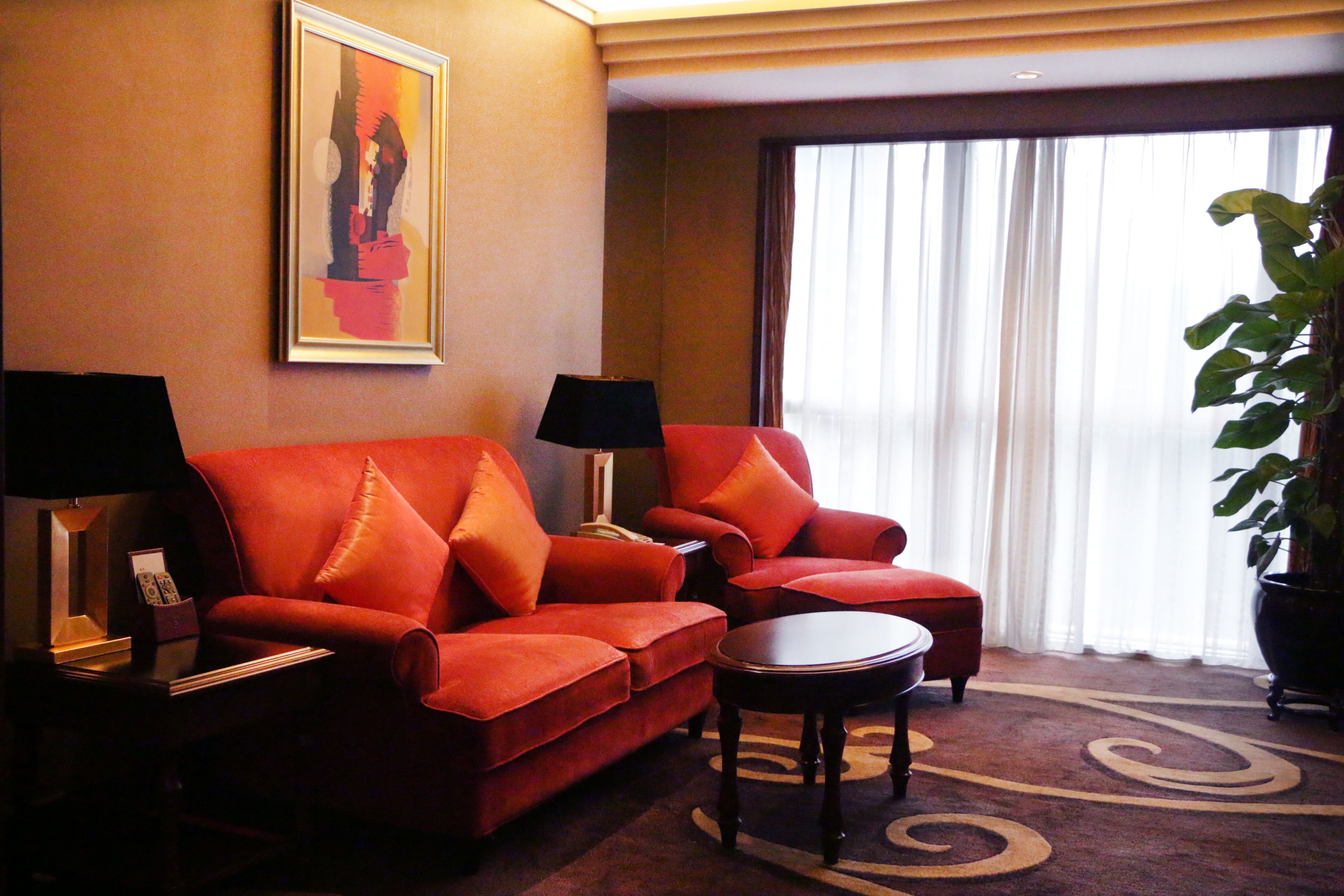 A hotel room with a red sofa, two armchairs, a small table, and a large potted plant.