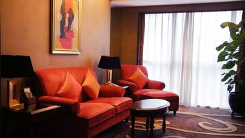 A hotel room with a red sofa, two armchairs, a small table, and a large potted plant.