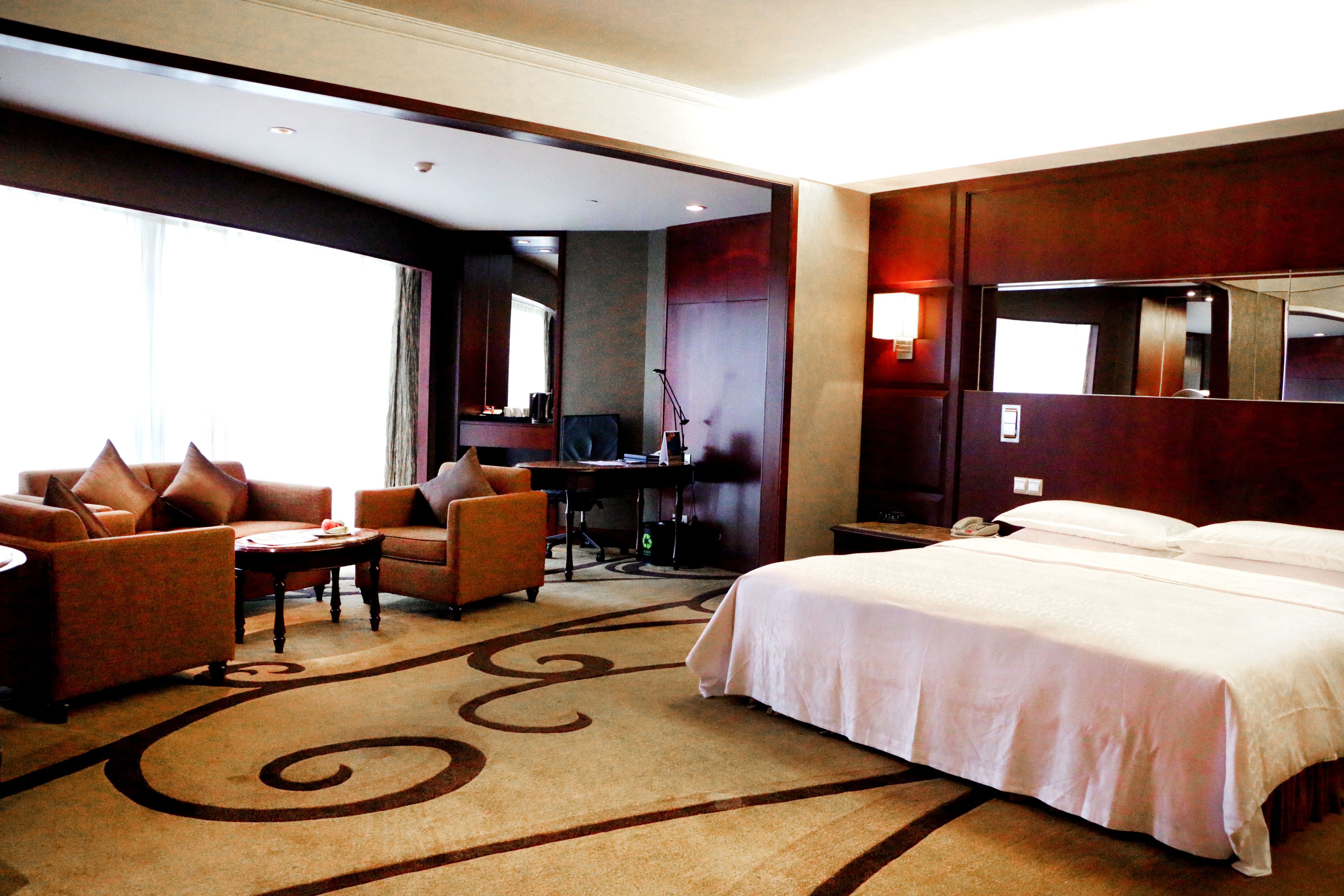 A hotel room with a large bed, two armchairs, a desk, and a large mirror.